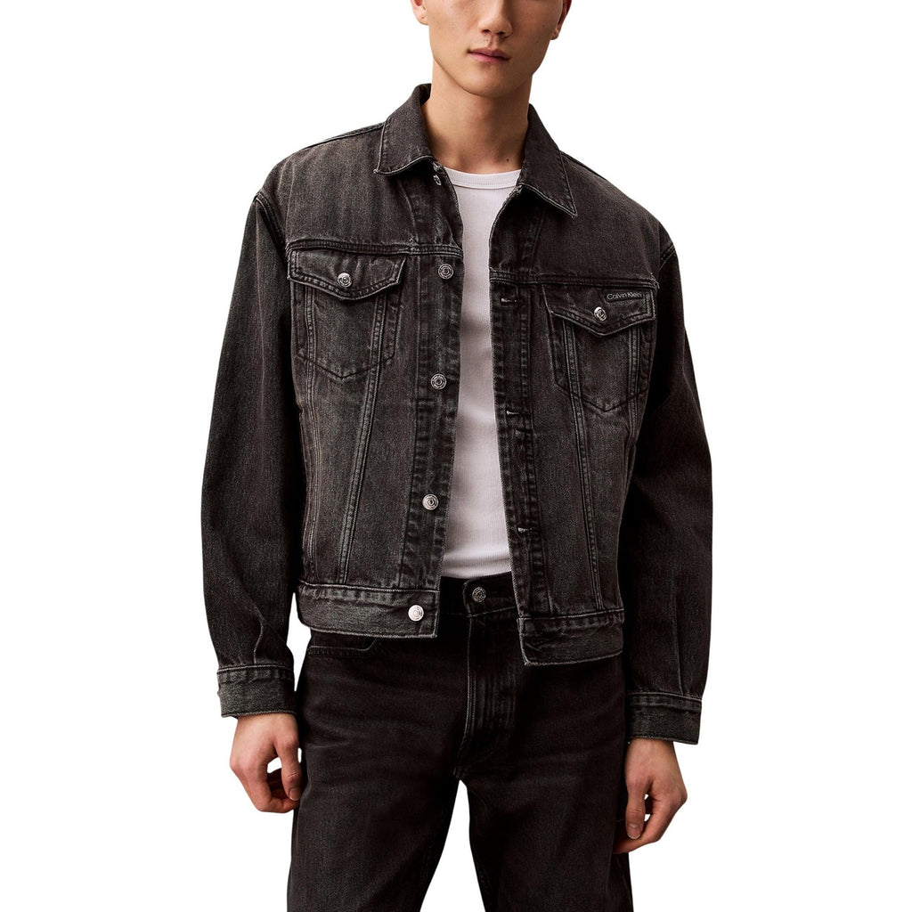 Lifestyle shot of a black denim jacket featuring button closure and chest pockets against a white background.