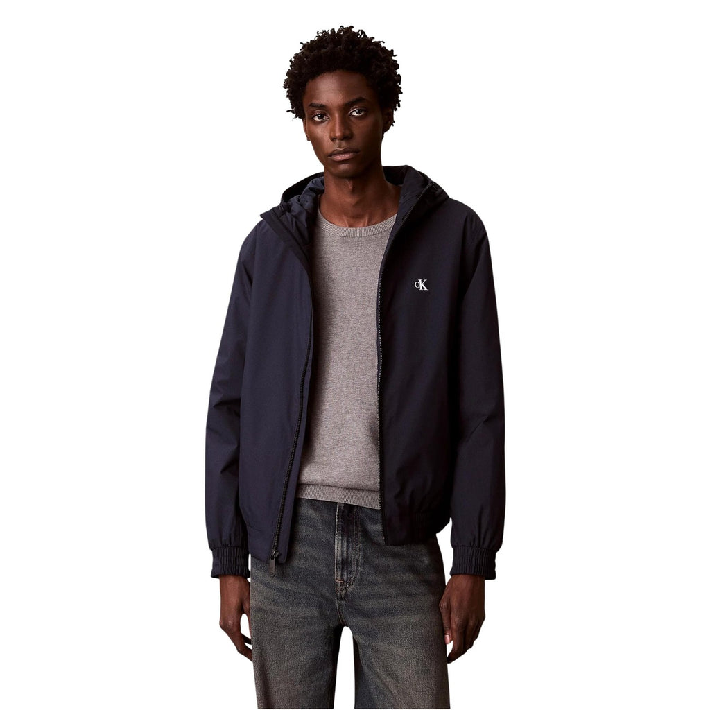 Lifestyle shot of a man wearing a navy blazer with a hood and zipper closure in a studio setting.
