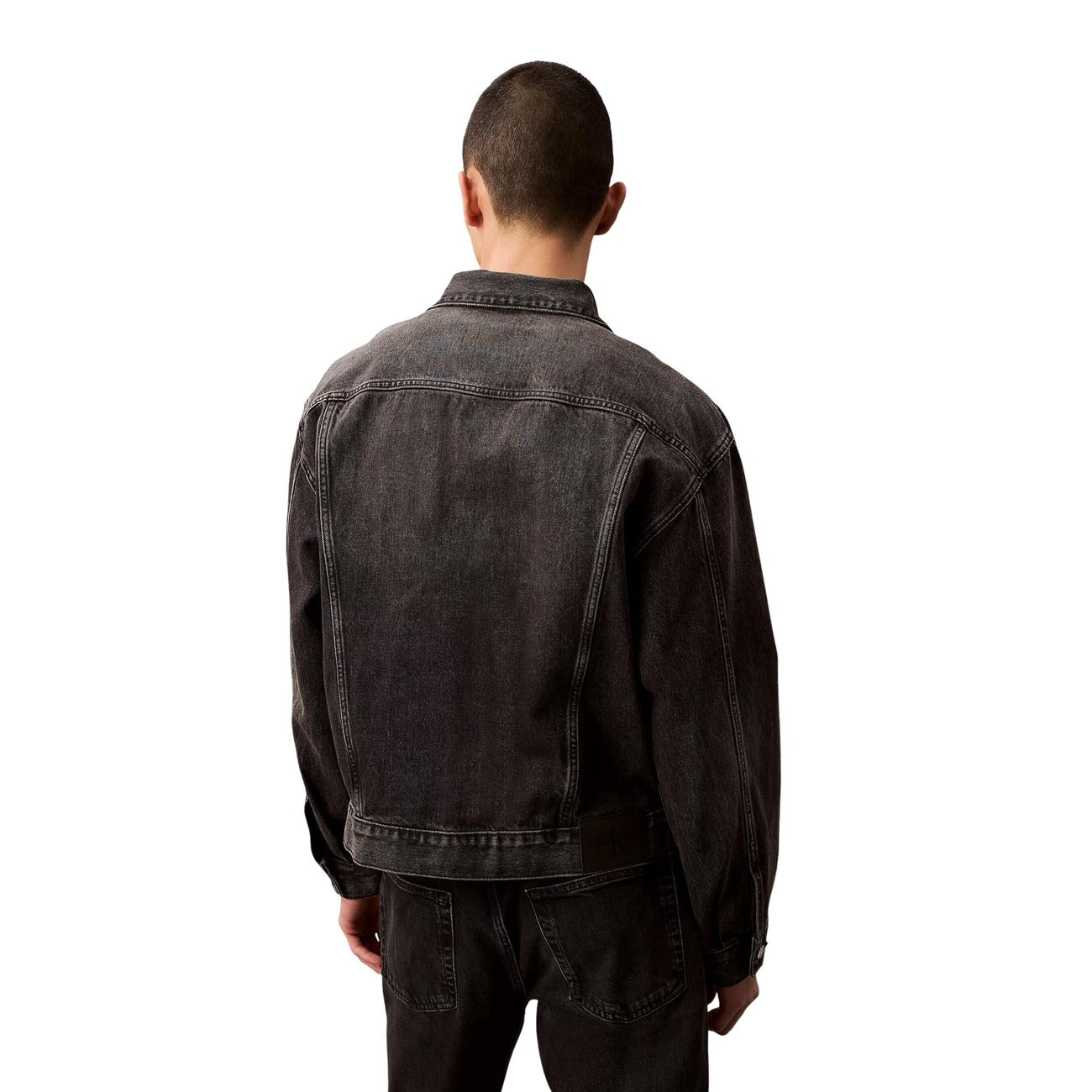 Back view of a black denim jacket showcasing seam details and back yoke on a white background.