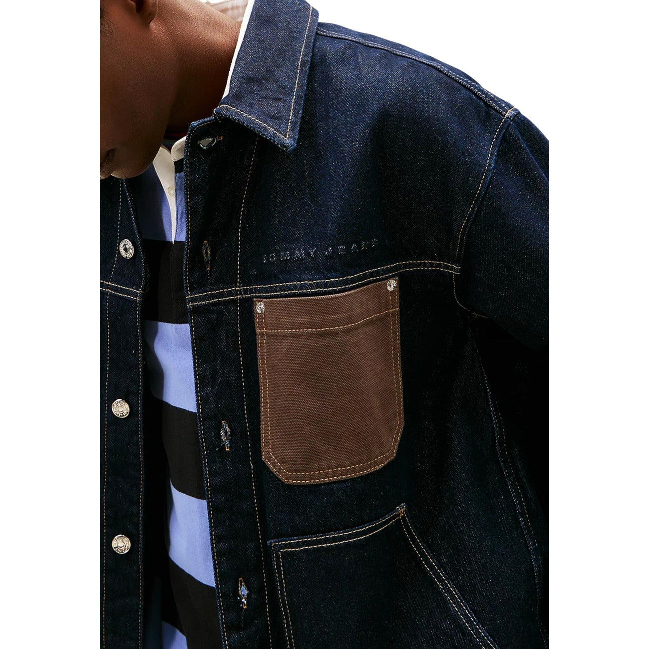 Close-up detail of a blue denim jacket highlighting chest pocket and stitching details.