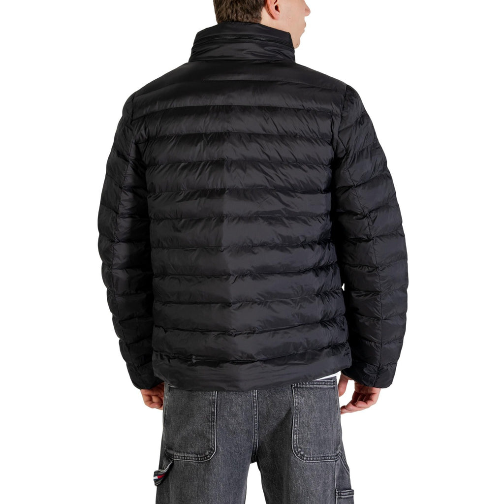 Back view of a man wearing a black puffer jacket with zipper closure and pockets in a studio setting.