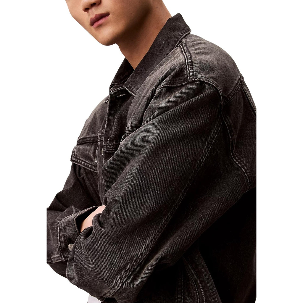Side view of a black denim jacket with long sleeves and a relaxed fit displayed on a white background.