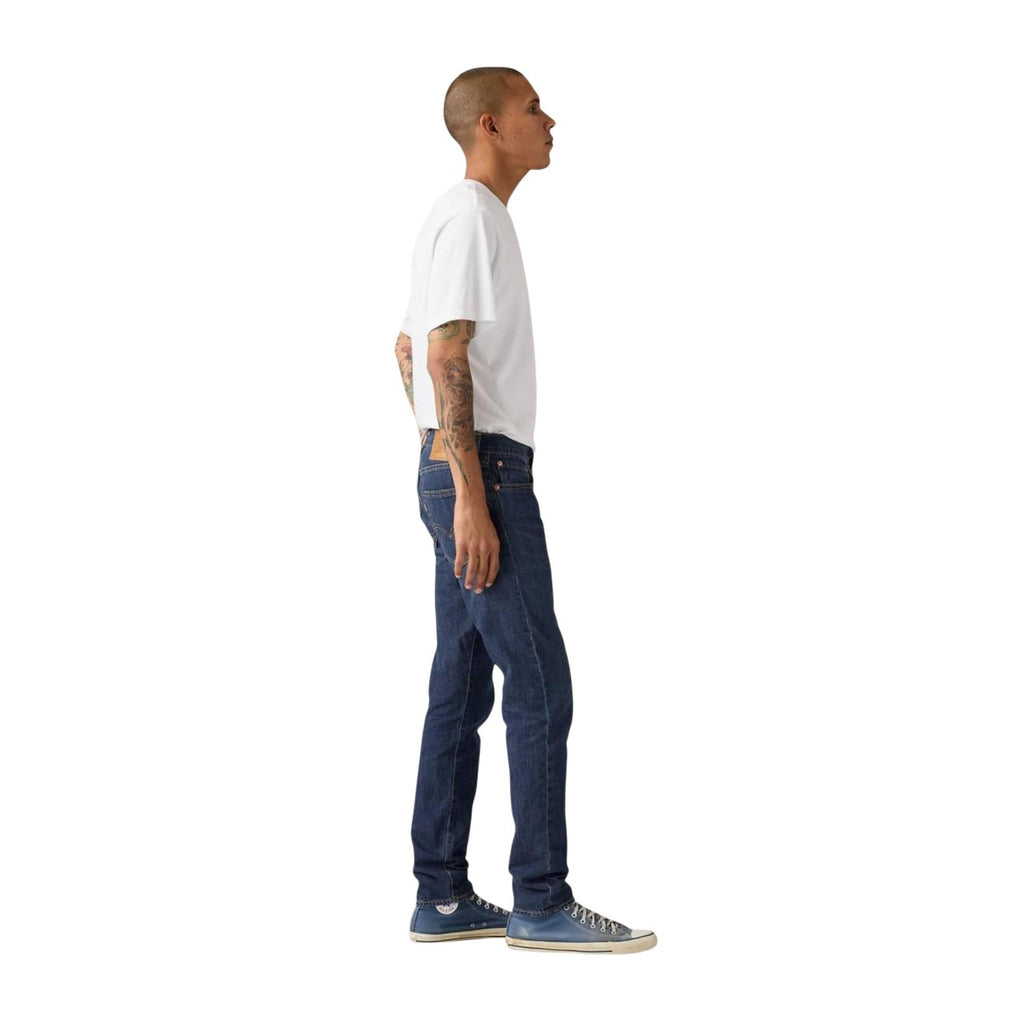 Side view of blue jeans showcasing slim fit and five pockets on a white background.