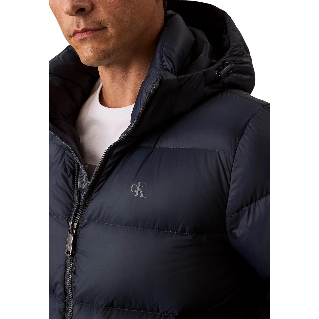 Detail close-up of a navy puffer jacket highlighting the hood, zipper closure, and logo on a white background.