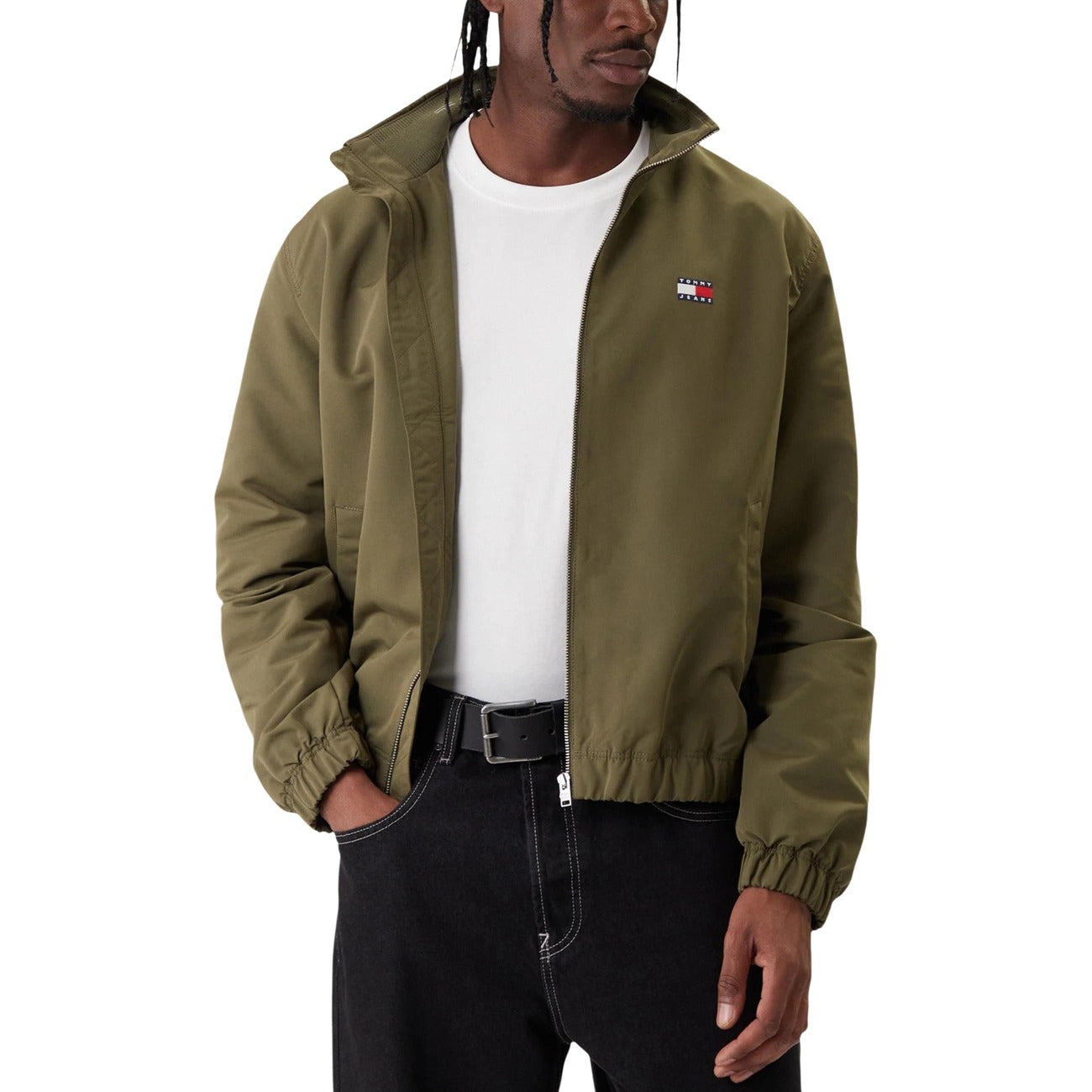 Detail close-up of the olive green jacket featuring a zipper closure and logo patch on a white background.