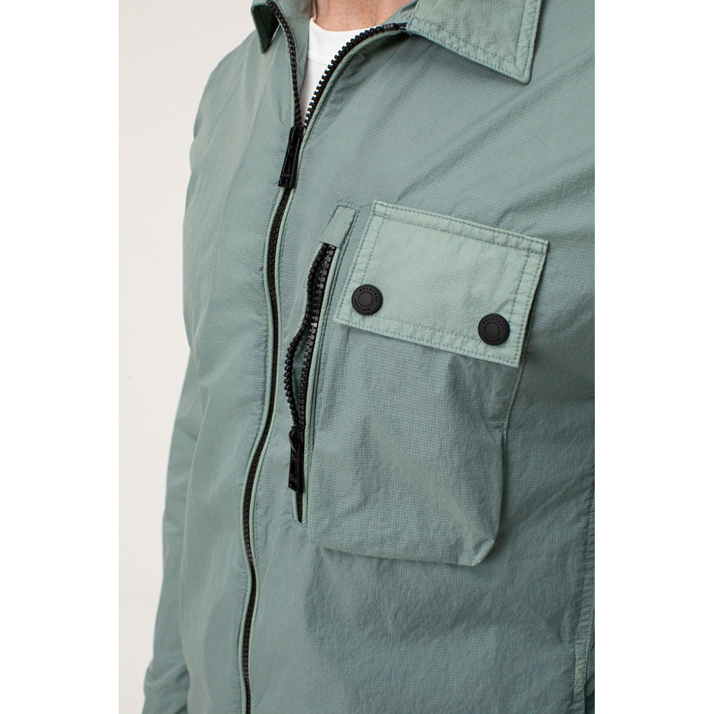 Close-up detail of the green Belstaff blazer pocket showcasing button closure and stitched detail.