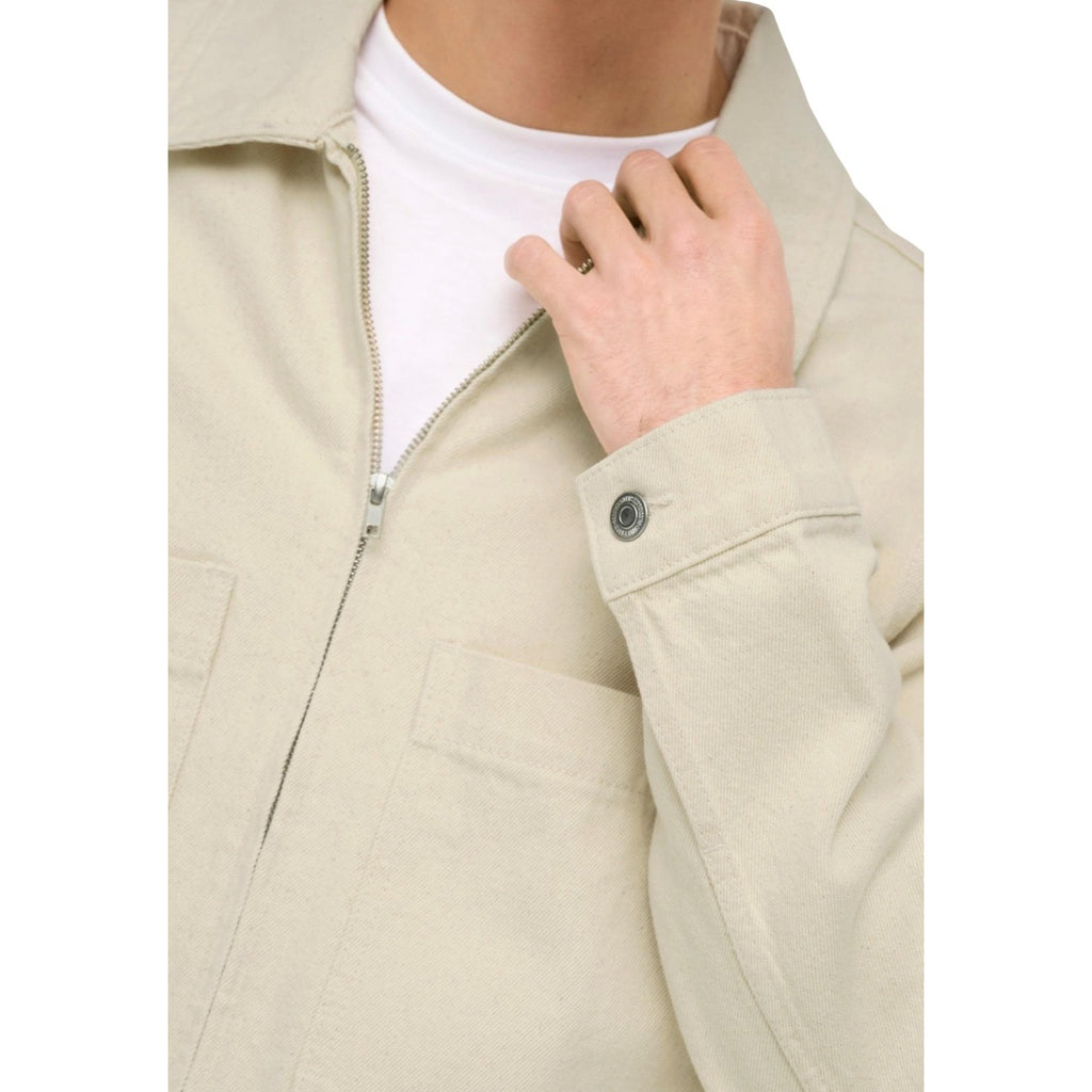 Detail close-up of a beige jacket showcasing zipper, button, and fabric texture on a white background.