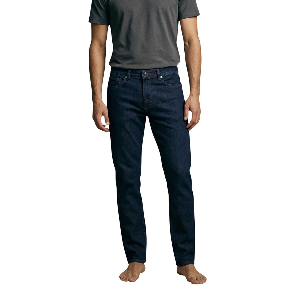 Lifestyle shot of a man wearing navy blue jeans in a casual style, barefoot, with gray elements in the background