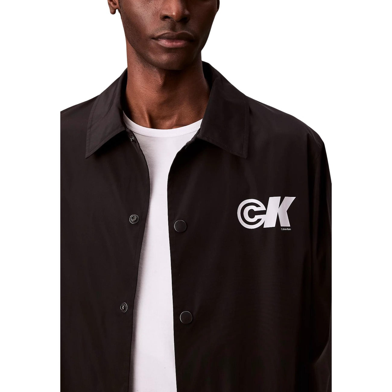 Detail close-up of a black blazer highlighting the logo patch and button closure on a white background.