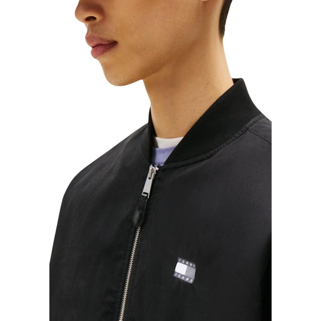 Close-up detail of the black bomber jacket highlighting the logo detail on a white background.