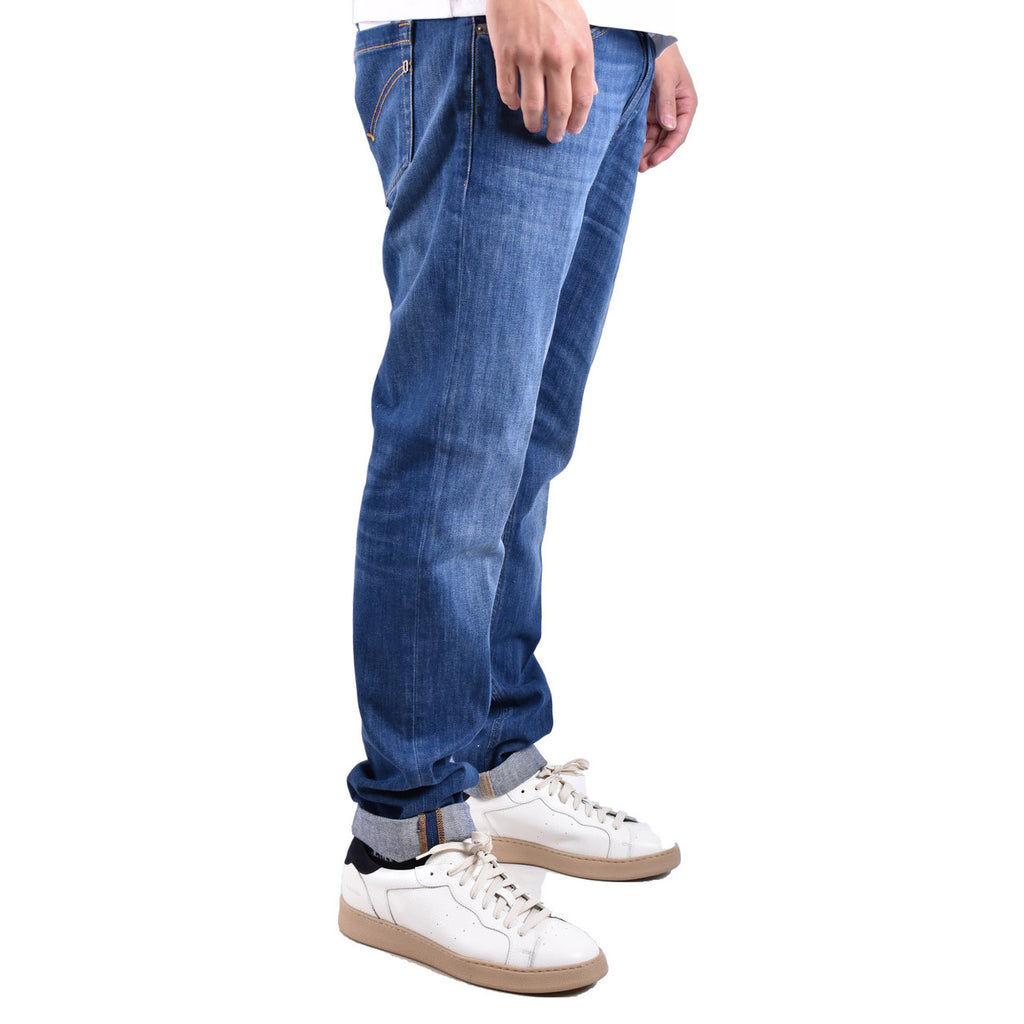 Side view of a person in blue Dondup jeans showcasing a slim fit and rolled cuffs in a studio environment.