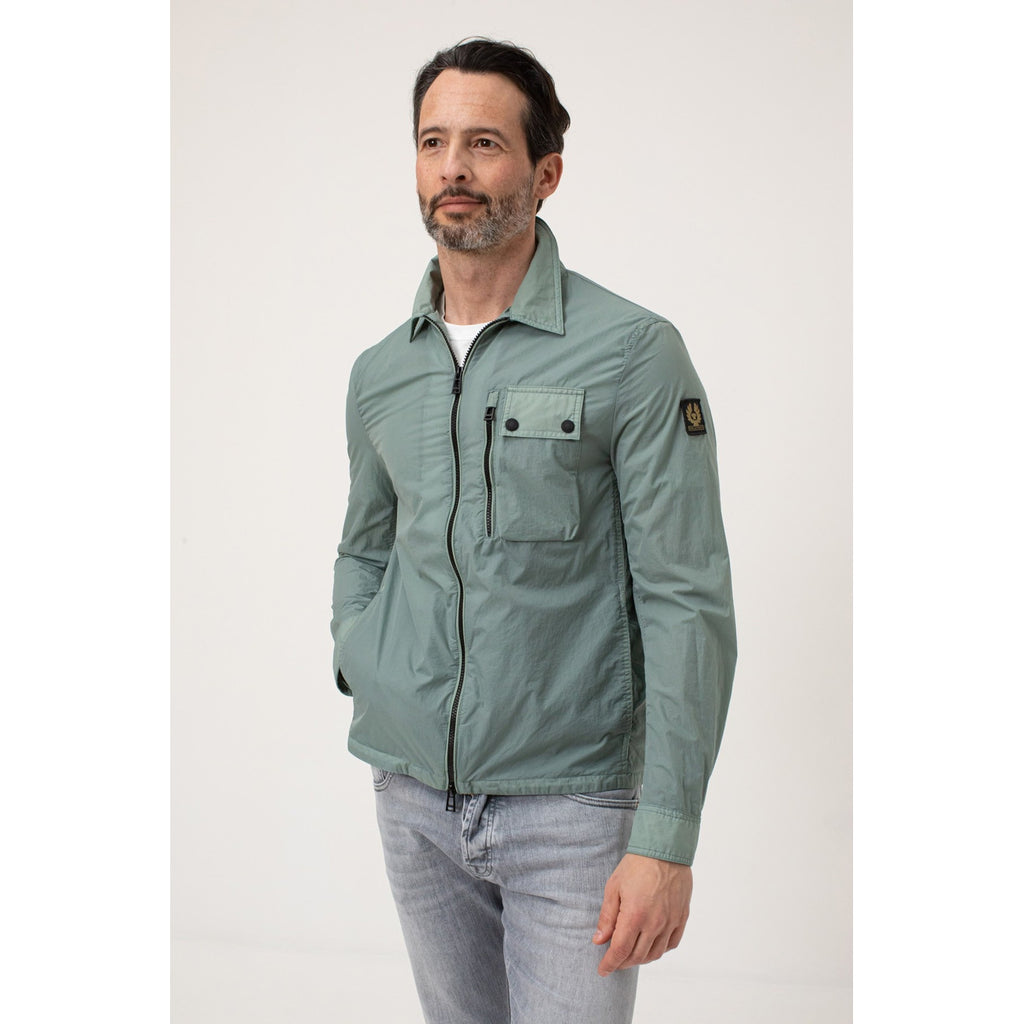 Lifestyle shot of a man wearing a green Belstaff blazer with a buttoned collar and pocket detail.