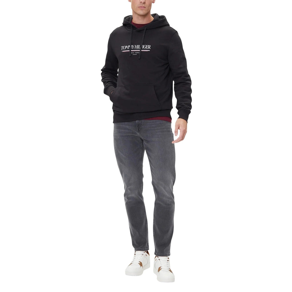 Lifestyle shot of a model wearing gray jeans with a black hoodie and sneakers on a white background