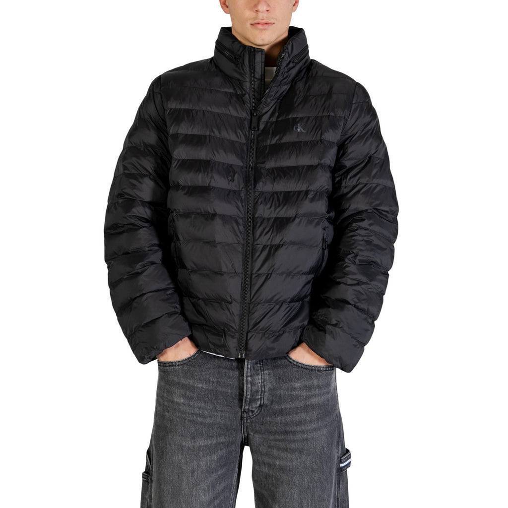 Lifestyle shot of a man wearing a black puffer jacket with zipper closure and pockets in a studio setting.