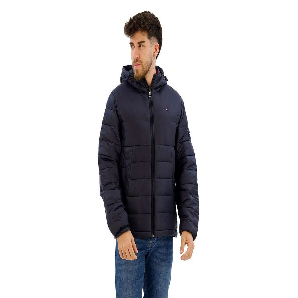 Lifestyle shot of a man wearing a navy puffer jacket with a hood and zipper closure on a white background.